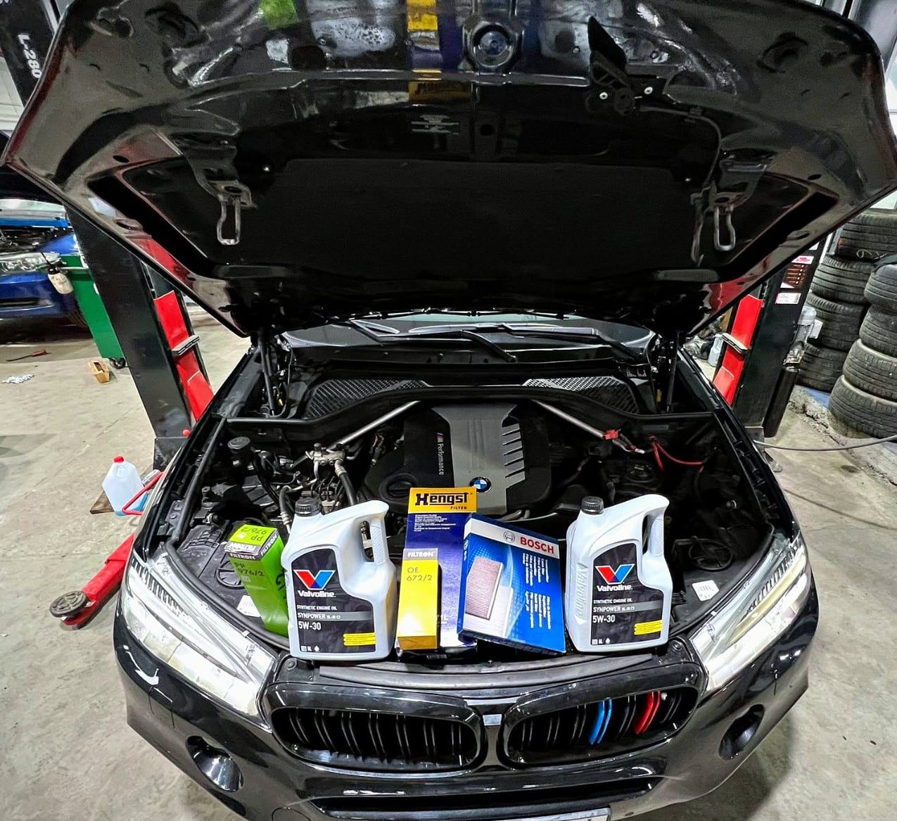 BMW z otwartą maską, przed autem oleje i filtry przygotowane do serwisu